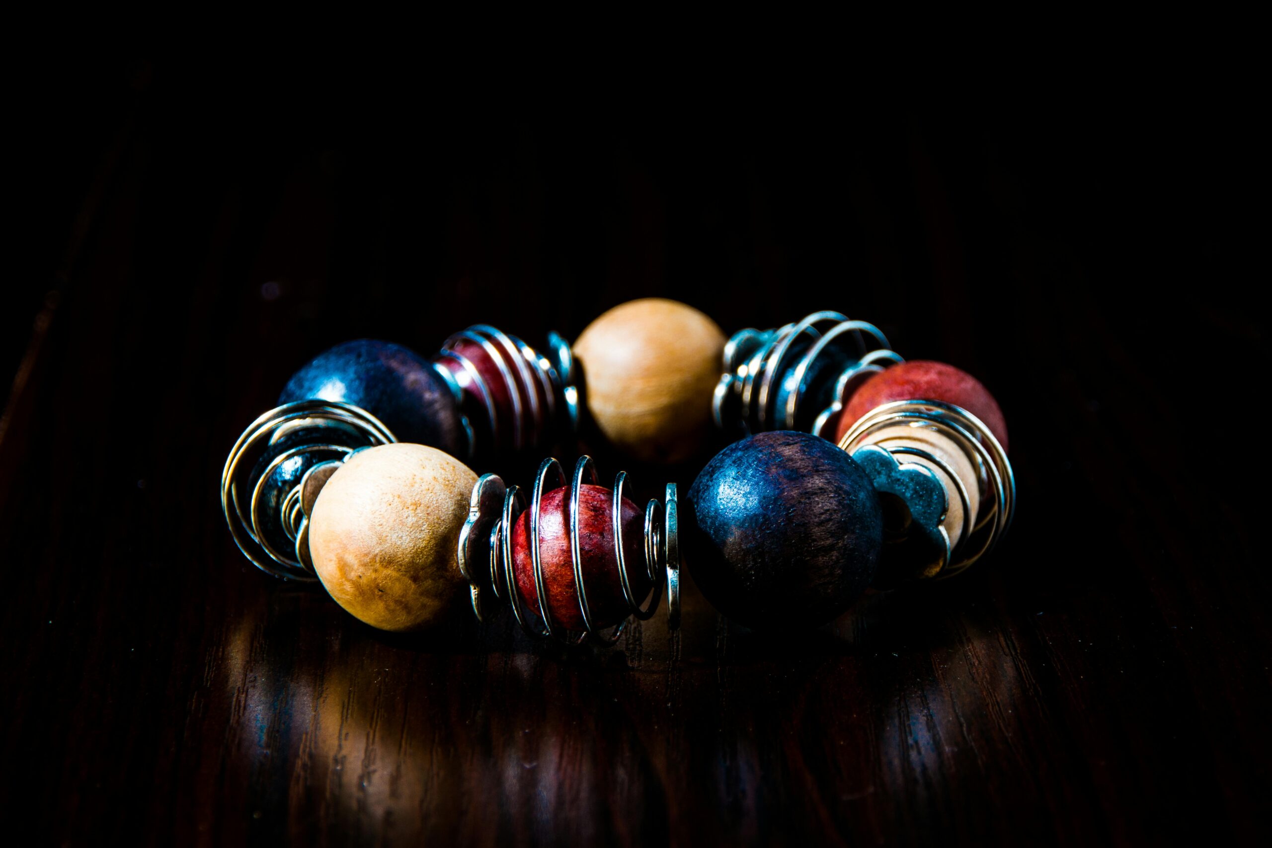 Close-up of a vibrant wood bead bracelet with metallic spiral accents on a dark background.